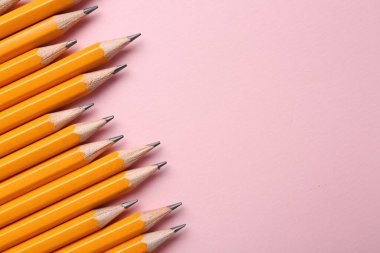 Pembe arka planda keskin grafit kalemler, düz yatış. Metin için boşluk
