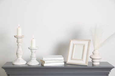 Beyaz duvarın yanındaki şöminede yanan mumlar ve diğer dekorlarla süslü şamdanlar.