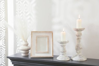 Beyaz duvarın yanındaki şöminede yanan mumlar ve diğer dekorlarla süslü şamdanlar.