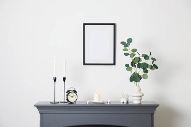 Beyaz duvarın yanındaki şöminede yanan mumlar, diğer dekor ve çalar saat ile şık şamdanlar.