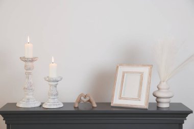 Beyaz duvarın yanındaki şöminede yanan mumlar ve diğer dekorlarla süslü şamdanlar.