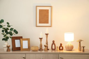 Havalı şamdanlar, yanan mumlar ve kapalı alandaki bej duvarın yanındaki dolaptaki diğer dekorlar.