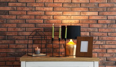 Mum ve tuğla duvarın yanındaki masada yanan mumlar.