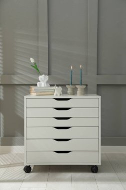 Gri duvarın yanındaki çekmecelerin üzerinde yanan mumlar olan şamdanlar.