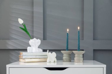 Gri duvarın yanındaki çekmecelerin üzerinde yanan mumlar olan şamdanlar.