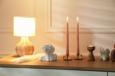Beyaz duvarın yanındaki çekmecelerin üzerinde yanan mumlar olan şamdanlar.