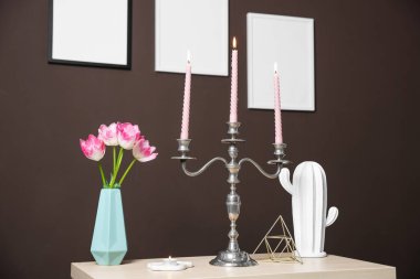 Kahverengi duvarın yanında yanan mumlar ve dekorlarla süslü zarif bir şamdan.