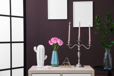 Kahverengi duvarın yanındaki dolapta yanan mumlar ve dekorlar olan zarif bir şamdan.