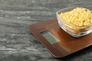 Modern elektronik mutfak terazisi, bir kase çiğ makarna ve gri mermer masa, yakın plan. Metin için boşluk