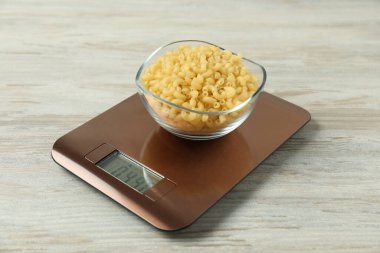 Modern elektronik mutfak terazisi, ahşap masada çiğ makarna, yakın plan.