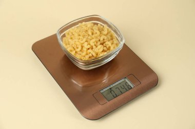 Bej arka planda bir kase çiğ makarna ile elektronik mutfak terazisi, yakın plan.
