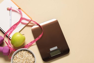 Elektronik mutfak ölçeği, mezura, not defteri ve bej masadaki ürünler, düz konum. Metin için boşluk