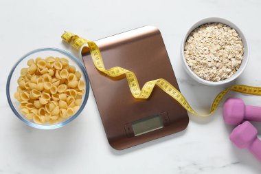 Elektronik mutfak ölçeği, mezura, halterler ve ürünler beyaz mermer masa üzerinde, düz zemin. Diyet