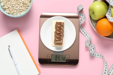 Elektronik mutfak ölçeği, mezura, not defteri ve pembe arka plandaki ürünler, düz konum. Kalori kontrolü
