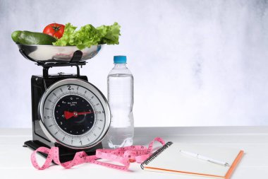 Mutfak pulları sebze, su, defter ve beyaz ahşap masa üzerindeki mezura.