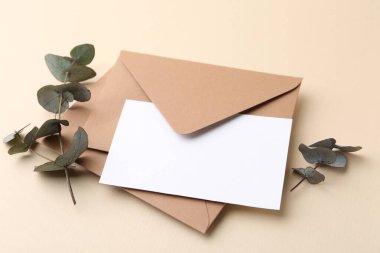Boş tebrik kartı, zarflar ve okaliptüs yaprakları bej arka planda, yakın plan