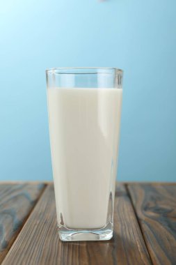 Açık mavi arka planda, cam bardakta taze süt, yakın plan.