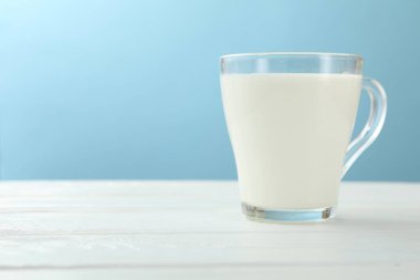 Cam bardaktaki taze süt beyaz ahşap masada açık mavi arka planda, yakın plan