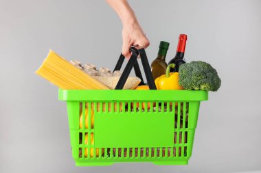 Elinde gri arka planda farklı ürünler olan alışveriş sepeti tutan adam, yakın plan.