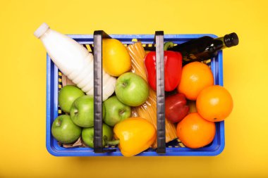 Sarı arka planda ürünlerle dolu plastik alışveriş sepeti.