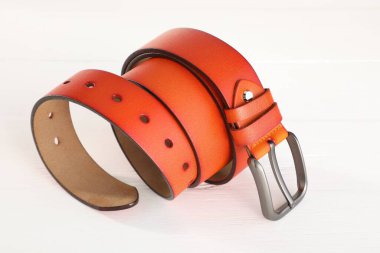 Beyaz ahşap masada turuncu bir deri kemer, yakın plan.