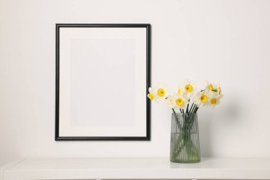 Beyaz masadaki vazodaki güzel nergisler ve kapalı alandaki resim çerçeveleri