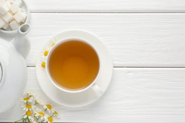 Fincanda nefis papatya çayı, taze çiçekler, şeker küpleri ve çaydanlık beyaz ahşap masa, düz yatak. Metin için boşluk