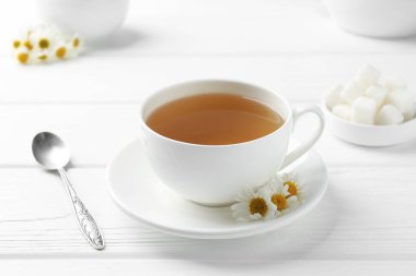 Fincanda nefis papatya çayı, taze çiçekler, şeker küpleri ve beyaz tahta masada kaşık, yakın plan.