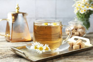 Cam bardakta nefis papatya çayı, taze çiçekler, kahverengi şeker ve çaydanlık ahşap masada, yakın plan.