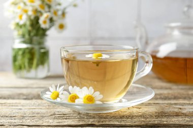 Cam bardakta nefis papatya çayı ve ahşap masada taze çiçekler, yakın plan.