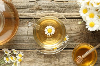 Cam bardakta nefis papatya çayı, taze çiçekler, bal ve çaydanlık ahşap masada, düz uzanmış