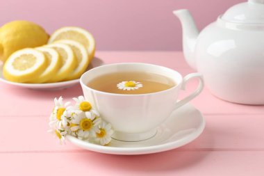 Fincanda nefis papatya çayı, taze çiçekler ve pembe ahşap masada limon, yakın plan.