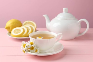 Fincanda nefis papatya çayı, taze çiçekler ve pembe ahşap masada limon, yakın plan.