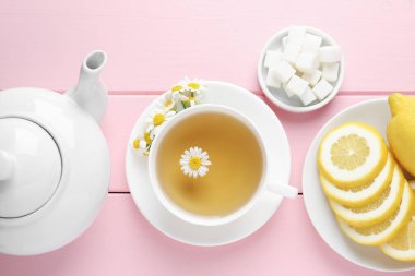 Fincanda nefis papatya çayı, taze çiçekler, şeker küpleri ve pembe ahşap masada limon.