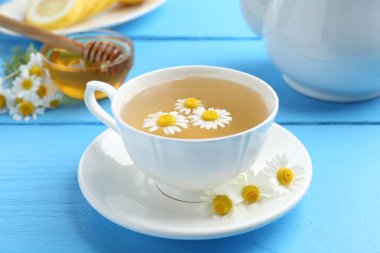 Fincanda nefis papatya çayı, taze çiçekler ve açık mavi ahşap masada bal, yakın plan.