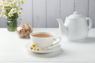 Fincanda lezzetli papatya çayı, taze çiçekler ve beyaz ahşap masada kahverengi şeker.