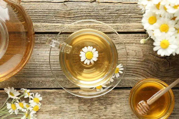 Cam bardakta nefis papatya çayı, taze çiçekler, bal ve çaydanlık ahşap masada, düz uzanmış