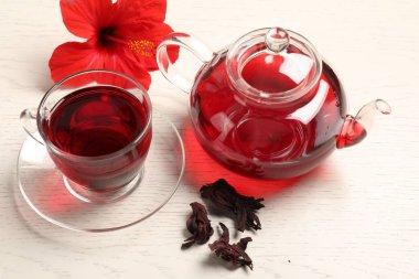 Cam fincanda lezzetli amber çayı, çaydanlık, kuru roselle sepals ve açık ahşap masada çiçek.