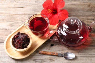 Cam fincanda lezzetli amber çayı, çaydanlık, kuru roselle sepals ve ahşap masada çiçek.