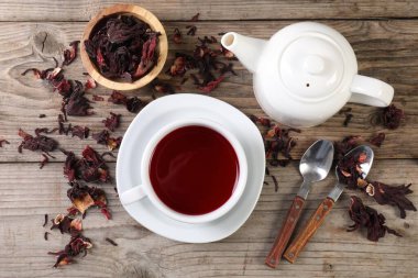 Lezzetli amber çayı fincanda, çaydanlıkta, kuru roselle sepals ve kaşıklar ahşap masada, düz yerde.