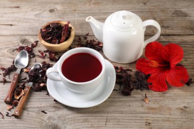 Lezzetli amber çayı fincanda, çaydanlıkta, kuru roselle sepals ve ahşap masada çiçek