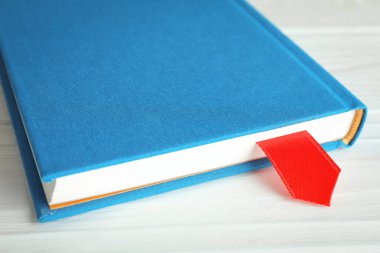 Beyaz ahşap masa üzerinde kırmızı kurdele yer imi olan kitap, yakın plan.