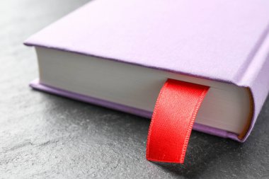 Koyu desenli masa üzerinde kırmızı kurdele yer imi olan kitap, yakın plan.