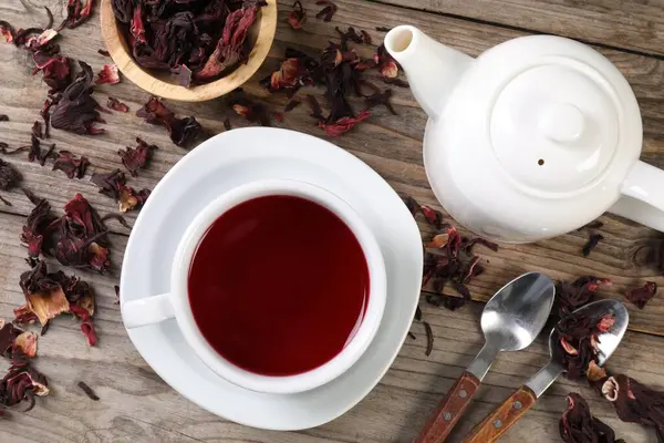 Lezzetli amber çayı fincanda, çaydanlıkta, kuru roselle sepals ve kaşıklar ahşap masada, düz yerde.