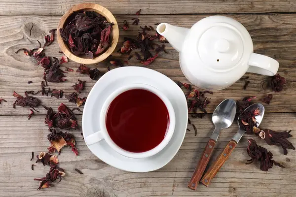 Lezzetli amber çayı fincanda, çaydanlıkta, kuru roselle sepals ve kaşıklar ahşap masada, düz yerde.
