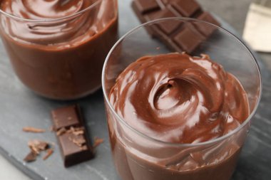 Lezzetli puding ve çikolata parçaları gri masada, yakın plan.