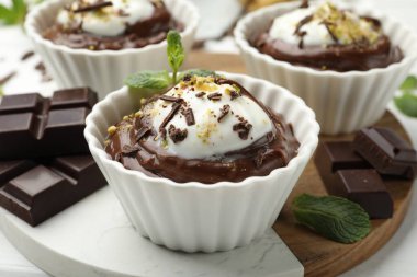 Krem şantili lezzetli puding ve beyaz ahşap masadaki çikolata parçaları, yakın plan.