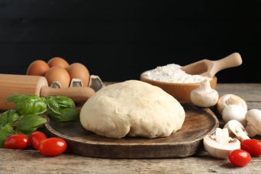 Pizza yapıyorum. Ahşap masadaki farklı malzemeler siyah arka plana karşı, yakın plan.