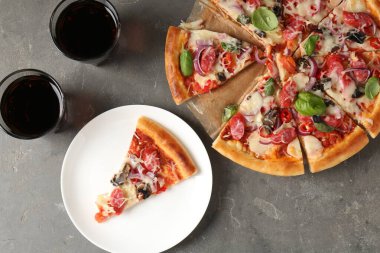 Gri masada servis edilen ince tütsülenmiş sosisli lezzetli bir pizza.