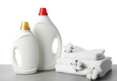 Beyaz arkaplana karşı gri masada yumuşatıcı, pamuk çiçeği ve havlu şişeleri